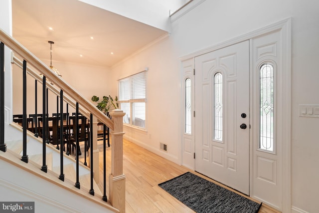 foyer entrance with stairs, crown molding, light wood-style floors, a chandelier, and baseboards