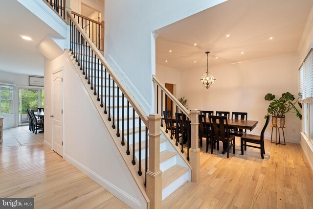 staircase featuring wood finished floors, a chandelier, baseboards, recessed lighting, and ornamental molding