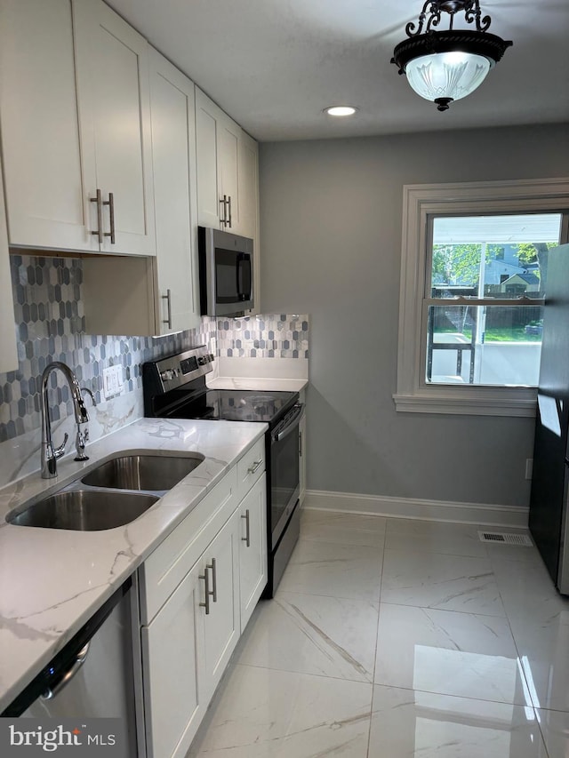kitchen featuring stainless steel appliances, a sink, tasteful backsplash, white cabinets, and light stone countertops