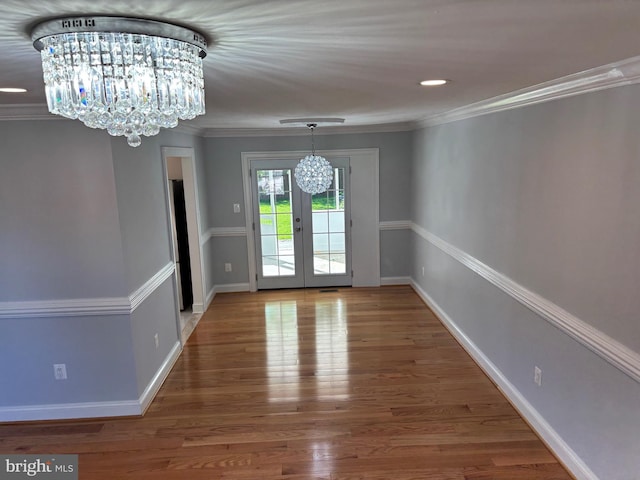 unfurnished dining area featuring a chandelier, french doors, wood finished floors, baseboards, and ornamental molding