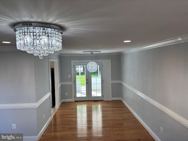 unfurnished dining area featuring a chandelier, wood finished floors, french doors, baseboards, and ornamental molding