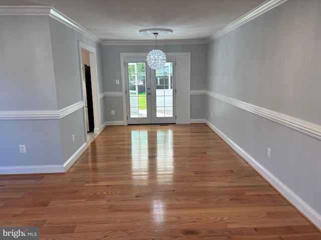 unfurnished dining area featuring a chandelier, wood finished floors, baseboards, french doors, and ornamental molding