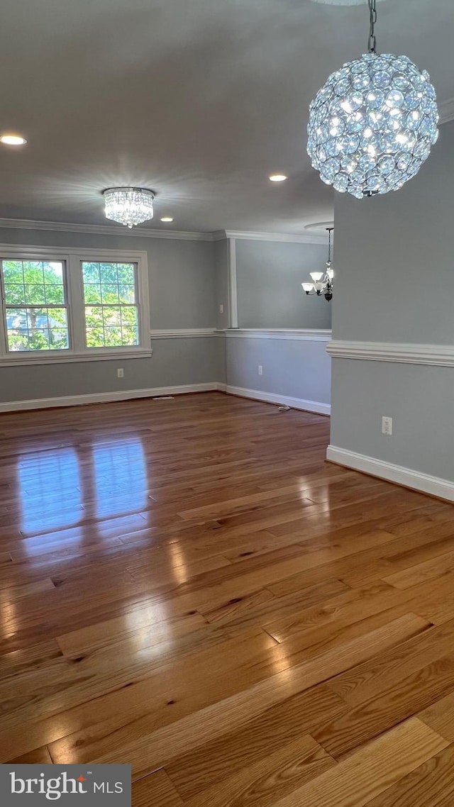 empty room featuring a chandelier, baseboards, wood finished floors, crown molding, and recessed lighting