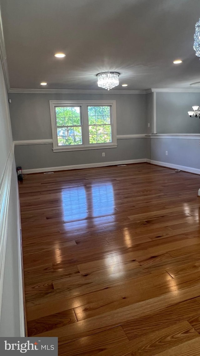 spare room featuring a chandelier, ornamental molding, baseboards, wood finished floors, and recessed lighting