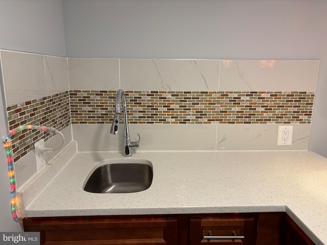 kitchen view of decorative backsplash, a sink, dark brown cabinetry, and light stone counters