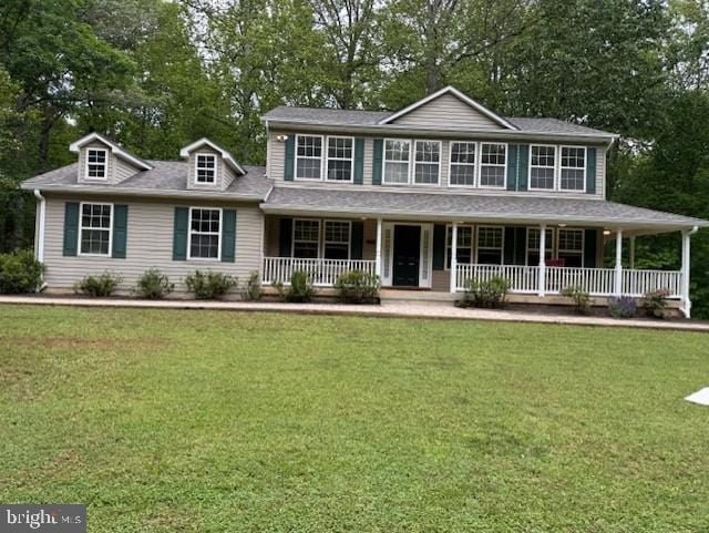 view of front of house with covered porch, a front yard, and view of wooded area