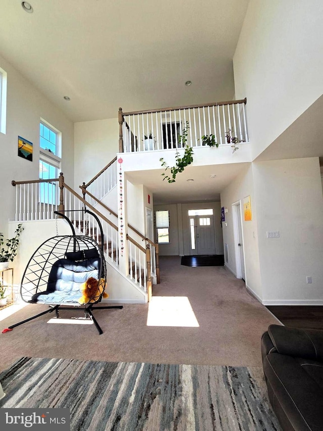unfurnished living room featuring stairs, a towering ceiling, plenty of natural light, baseboards, and carpet