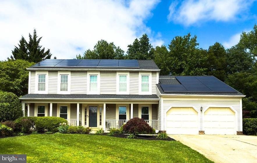 view of front of home featuring covered porch, roof mounted solar panels, an attached garage, concrete driveway, and a front yard