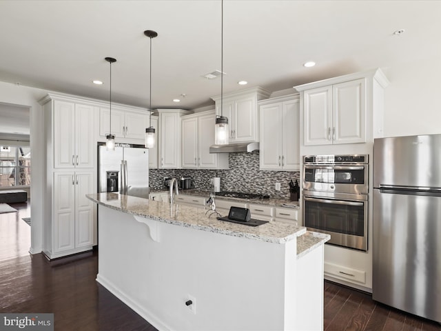 kitchen featuring appliances with stainless steel finishes, tasteful backsplash, white cabinetry, a center island with sink, and recessed lighting