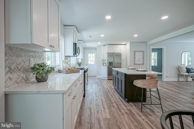 kitchen with appliances with stainless steel finishes, white cabinets, decorative backsplash, a kitchen bar, and recessed lighting