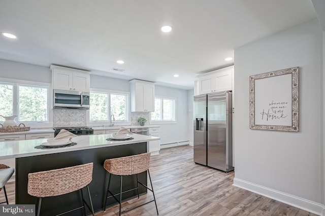 kitchen featuring appliances with stainless steel finishes, baseboard heating, a breakfast bar area, light countertops, and white cabinets
