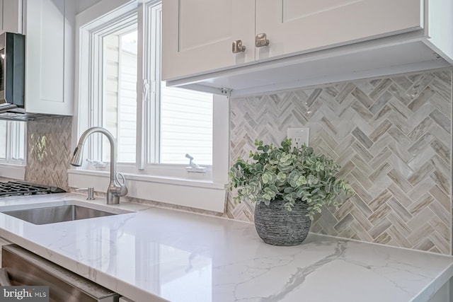 kitchen featuring tasteful backsplash, white cabinetry, light stone counters, stainless steel dishwasher, and a sink