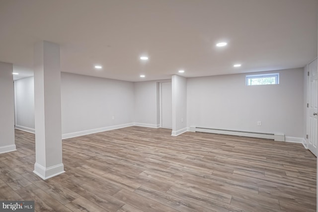 below grade area with a baseboard radiator, wood finished floors, recessed lighting, and baseboards
