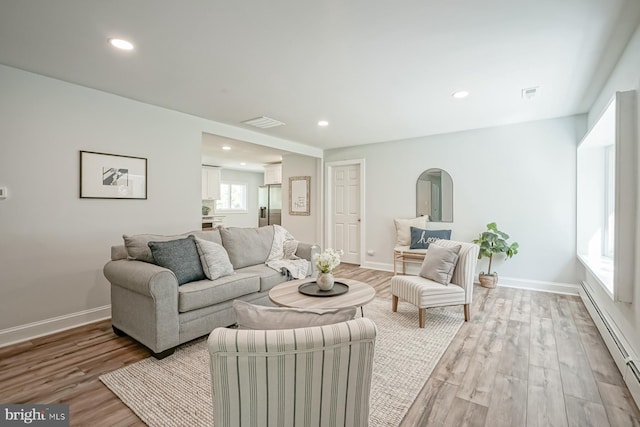 living room with baseboard heating, light wood-style flooring, baseboards, and recessed lighting
