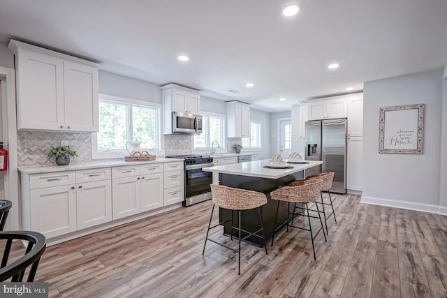 kitchen featuring appliances with stainless steel finishes, light wood-type flooring, a breakfast bar area, white cabinets, and backsplash