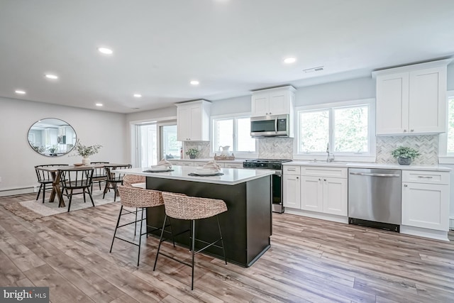 kitchen with appliances with stainless steel finishes, a sink, light wood-type flooring, tasteful backsplash, and a kitchen island