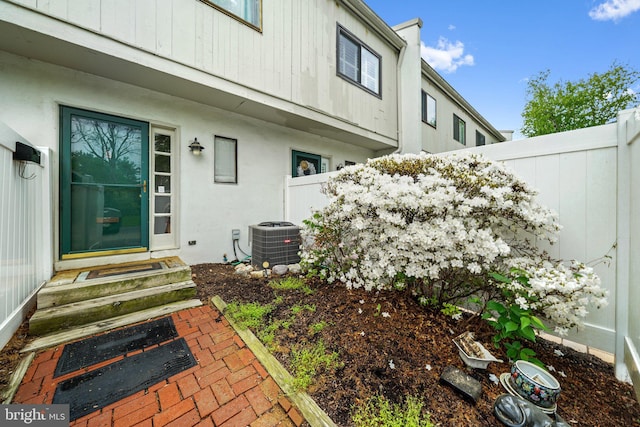 view of exterior entry with fence, stucco siding, and central AC unit