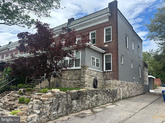 view of property exterior featuring stairway, a chimney, and a tile roof