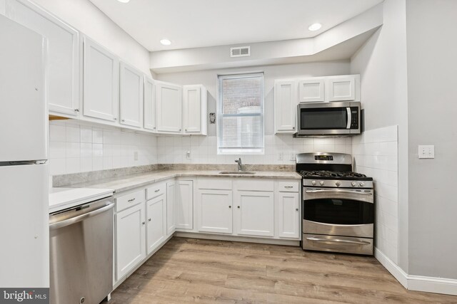 1609 N Hilton St, Baltimore, MD 21216 - kitchen featuring appliances with stainless steel finishes, white cabinetry, tasteful backsplash, light wood-type flooring, and recessed lighting