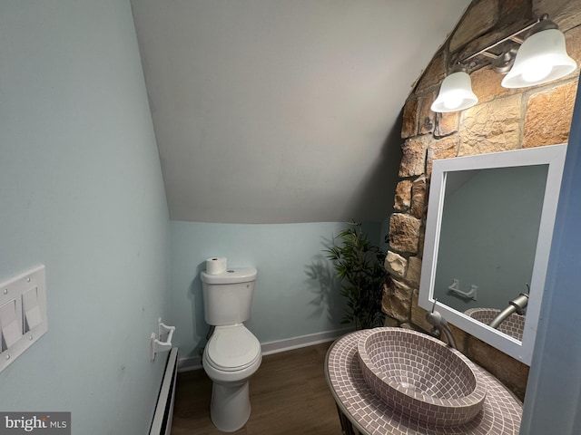 half bathroom with wood finished floors, toilet, lofted ceiling, a baseboard heating unit, and baseboards