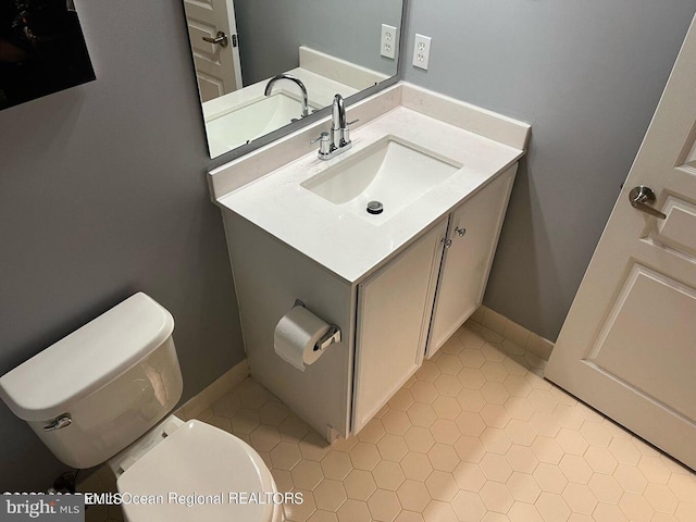 half bathroom with toilet, vanity, tile patterned floors, and baseboards
