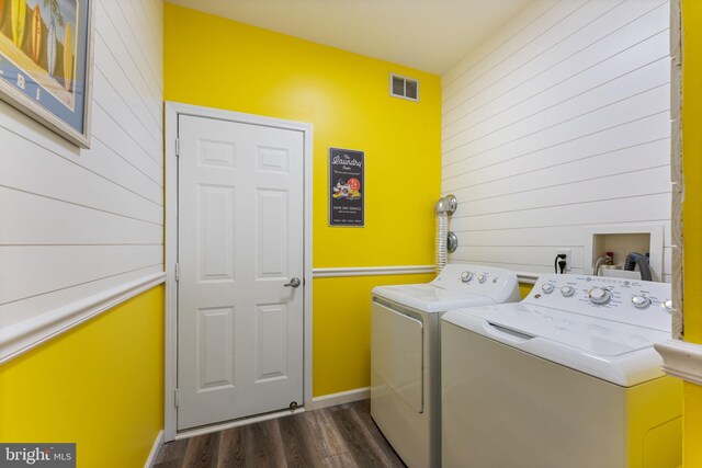 laundry area with washing machine and dryer, dark wood finished floors, wood walls, and baseboards