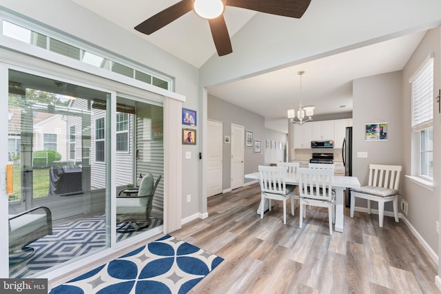 dining space featuring light wood finished floors, a ceiling fan, a chandelier, baseboards, and lofted ceiling