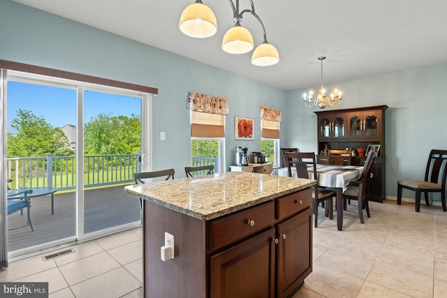 kitchen with hanging light fixtures, light tile patterned floors, a chandelier, light stone countertops, and a center island