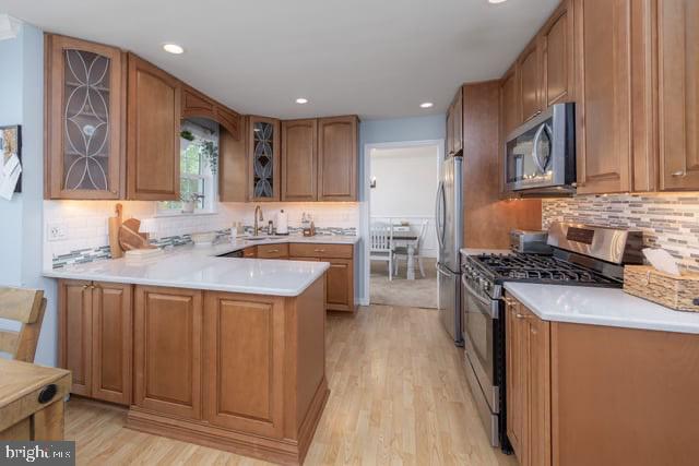 25 Aberdeen Dr, Sicklerville, NJ 08081 - kitchen with stainless steel appliances, light wood-type flooring, decorative backsplash, glass insert cabinets, and a peninsula