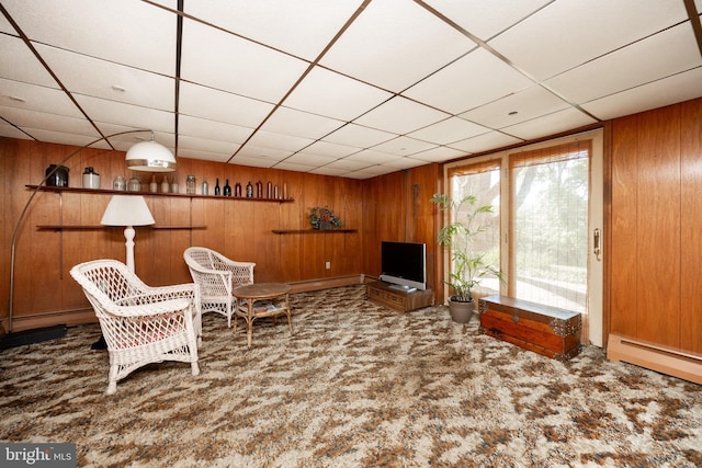 carpeted living area featuring wood walls, a drop ceiling, and a baseboard radiator