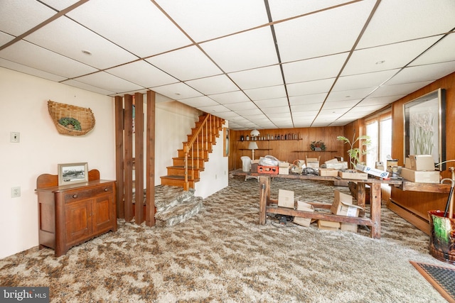 living room with carpet floors, stairway, a drop ceiling, and wood walls