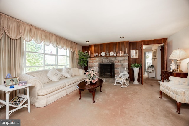 living room with light carpet, wood walls, and a stone fireplace