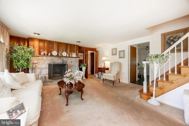 living room featuring stairway, a fireplace, baseboards, light carpet, and wood walls
