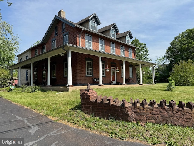 view of front of house featuring brick siding, covered porch, a chimney, and a front lawn