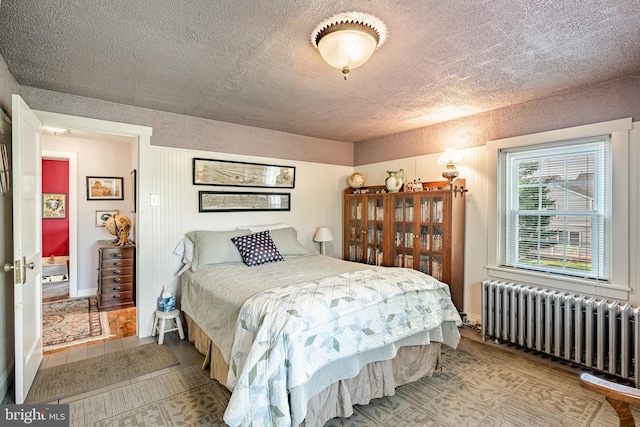 bedroom with radiator heating unit, a textured ceiling, and wood finished floors