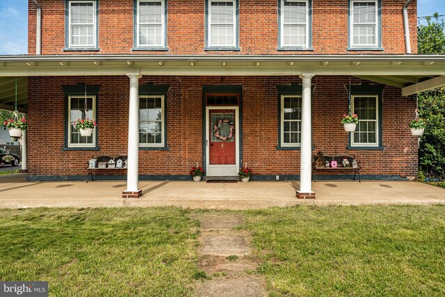 property entrance with covered porch, a lawn, and brick siding