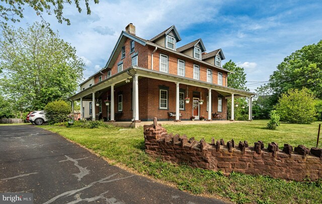 view of front of home featuring brick siding, a porch, a chimney, and a front lawn