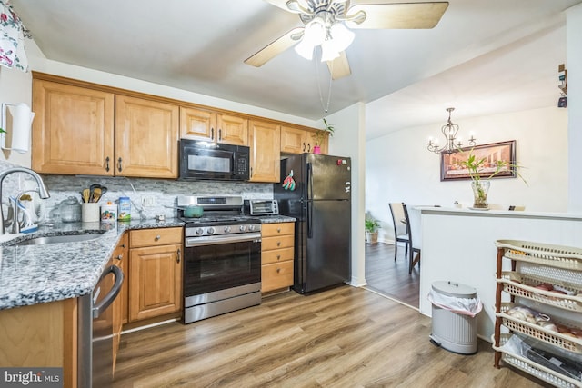kitchen with black appliances, a sink, light stone countertops, decorative backsplash, and light wood-type flooring