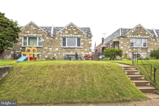 rear view of house with a lawn and stone siding