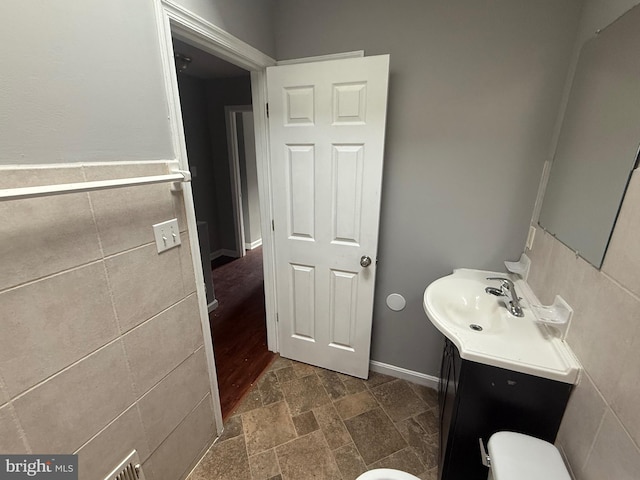 bathroom featuring vanity, stone finish flooring, toilet, and tile walls