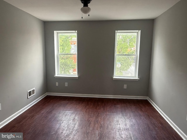 spare room featuring dark wood-style floors, plenty of natural light, baseboards, and a ceiling fan