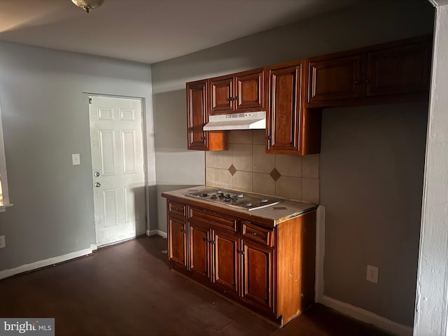 kitchen featuring under cabinet range hood, cooktop, tasteful backsplash, dark wood finished floors, and baseboards