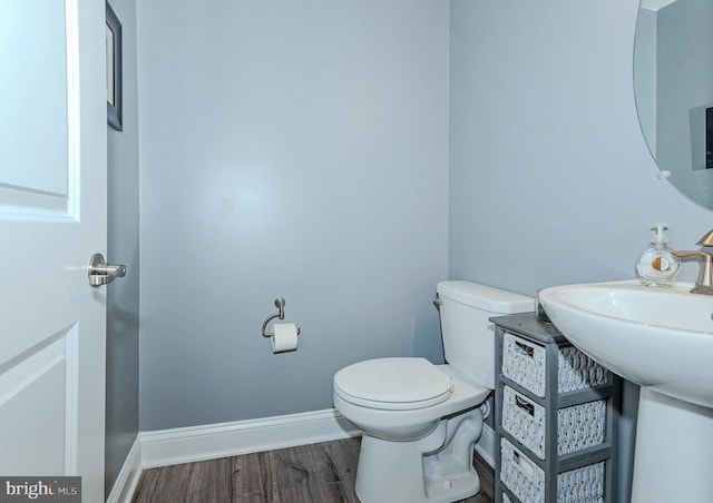 half bath with toilet, wood finished floors, and baseboards