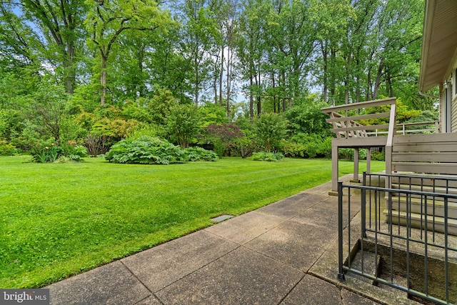 view of grassy yard featuring view of wooded area, a deck, and a patio area