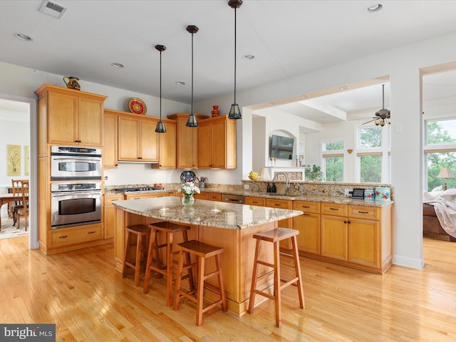 kitchen featuring a sink, light wood finished floors, appliances with stainless steel finishes, a kitchen bar, and a kitchen island