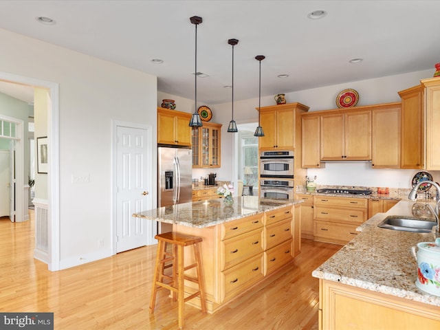 kitchen with stainless steel appliances, a sink, light wood finished floors, a center island, and a kitchen breakfast bar