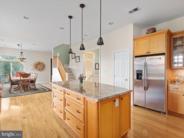 kitchen featuring stainless steel fridge, light wood finished floors, glass insert cabinets, light stone counters, and pendant lighting