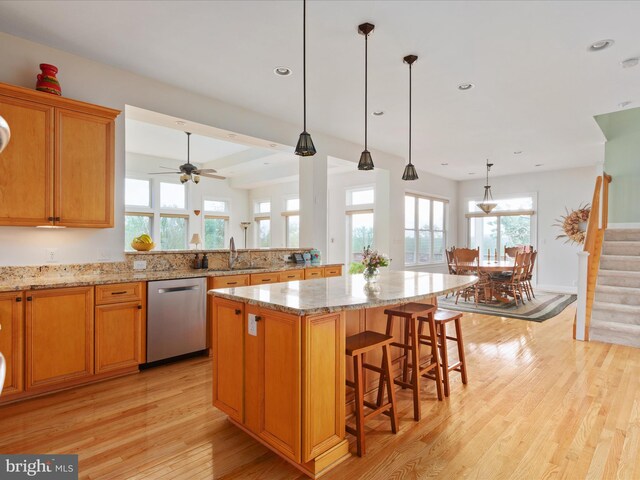 kitchen with stainless steel dishwasher, light wood-style flooring, a kitchen island, light stone countertops, and a breakfast bar