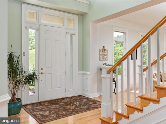 foyer with plenty of natural light, wood finished floors, stairway, crown molding, and wainscoting