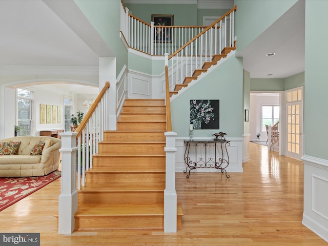 staircase featuring wood finished floors, arched walkways, ornamental molding, and a towering ceiling